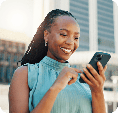 Mulher sorridente usando um smartphone em ambiente externo, transmitindo felicidade e conexão digital, com raios de sol e edifícios ao fundo.
