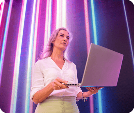 Mulher idosa analisando uma notebook com fundo de luzes neon coloridas, refletindo tecnologia e modernidade em ambiente contemporâneo.