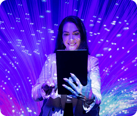 Mulher sorridente usando blazer interagindo com um tablet em ambiente com projeções de luz azul, representando tecnologia, inovação e tendências digitais.