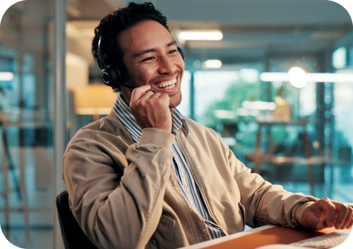 Homem sorridente usando fone de ouvido em ambiente de escritório, representando atendimento ao cliente ou suporte técnico.