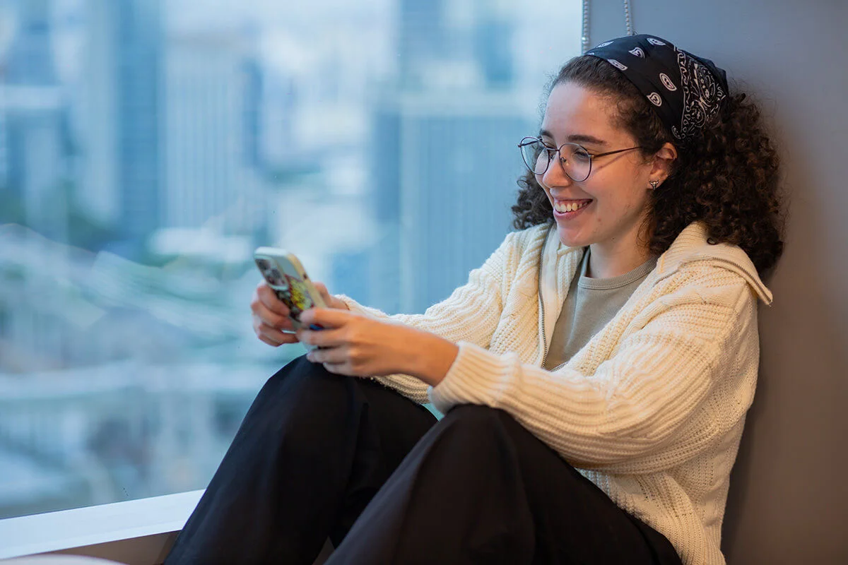 Mulher sentada olhando para celular e sorrindo