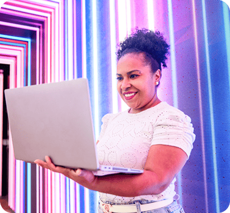 Mulher sorridente usando um laptop em um ambiente com iluminação de luzes neon coloridas, destacando-se a palavra-chave "trabalho remoto".