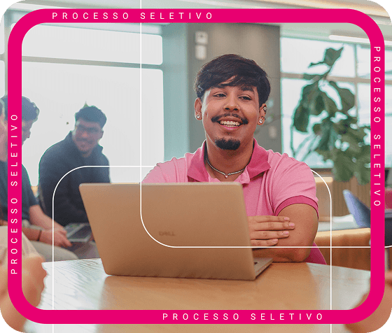 Homen moreno claro, com blusa rosa sentado com um computador a sua frente