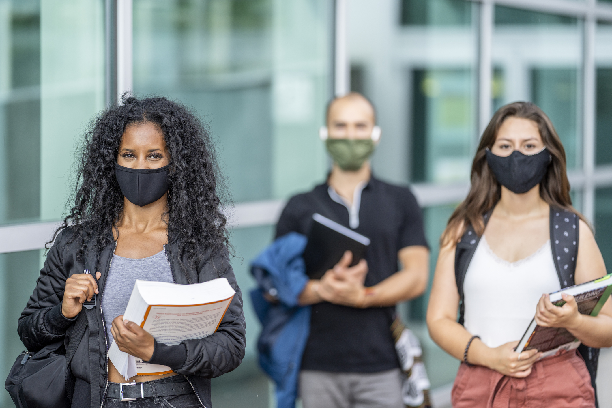 3 students of various ethnicities wearing protective face masks at school to protect from the transfer of germs.