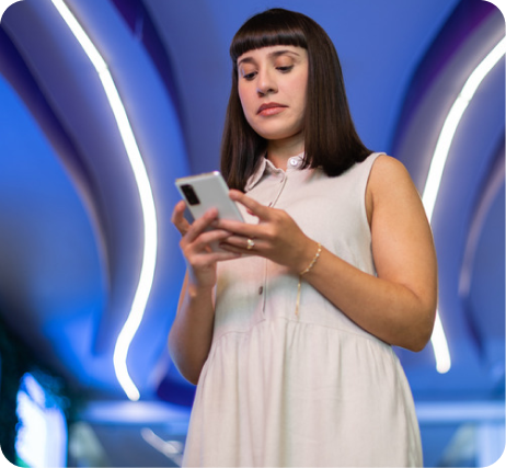 Jovem mulher usando vestido branco e cabelo desigual, concentrada ao usar celular em ambiente moderno com iluminação azul e arcos luminosos ao fundo.
