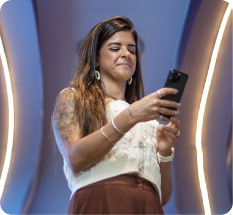 Mulher sorridente usando um celular, aparência animada e descontraída, cenário moderno com iluminação de destaque, transmitindo alegria e interação digital.