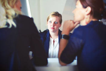 Dois empreendedores fazendo uma entrevista com candidata, que parece muito atenta e nervosa, em uma entrevista conduza-a adequadamente, ouvindo mais que falando.