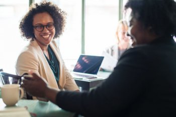 empreendedora sentada a mesa conversando com uma colaboradora e tomando um cafè