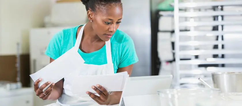 A imagem mostra uma mulher negra, folheando cartas que ela recebeu e vendo se o seu cliente pagou suas dívidas e saiu da inadimplência