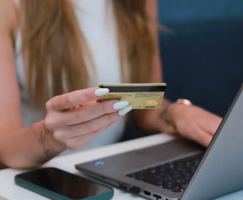 Mão de uma mulher segurando um cartão enquanto digita em um computador