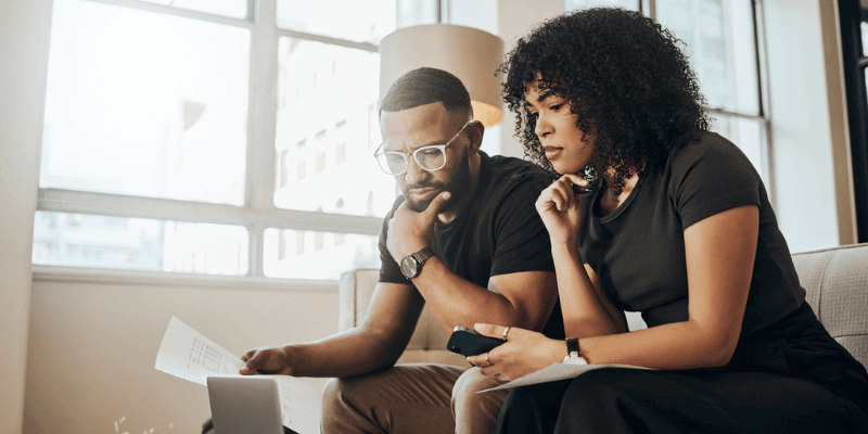 A imagem mostra um casal negro, heterossexual e que aparentam ser empreendedores, olhando para um laptop e realizando cálculos para entender se o empréstimo para mei que eles estão cotando é viável para o seu negócio.
